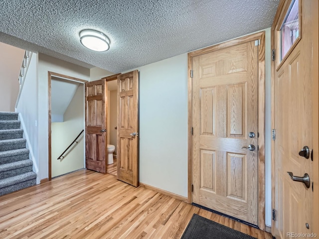 foyer entrance with light wood-type flooring, baseboards, stairway, and a textured ceiling