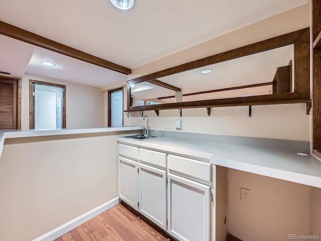 kitchen with light wood-style flooring, a sink, light countertops, white cabinetry, and beam ceiling