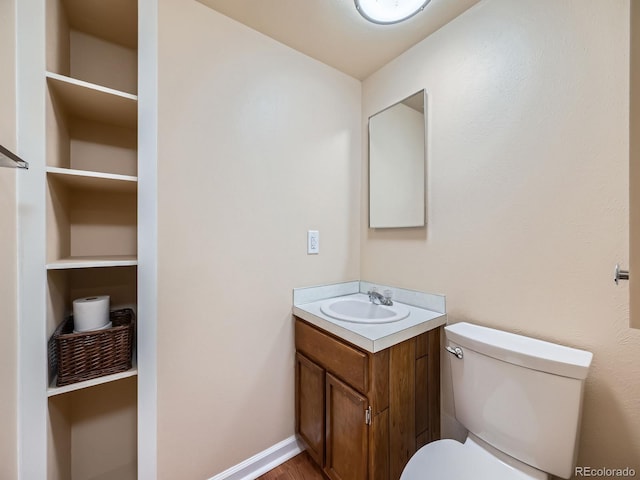 half bath featuring baseboards, vanity, and toilet