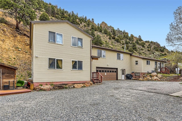 back of property with gravel driveway, a garage, and a wooden deck