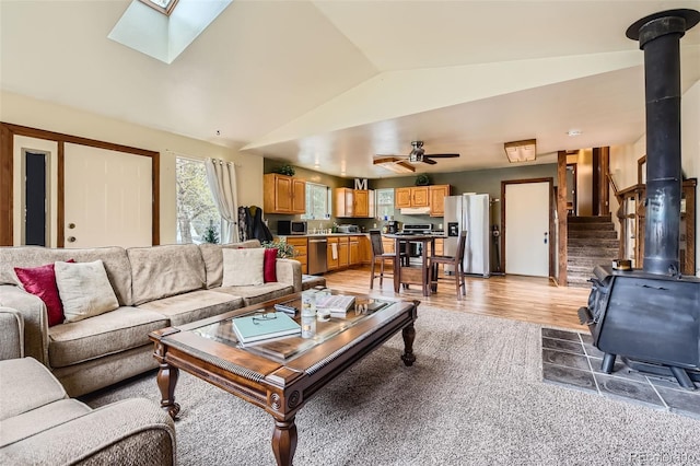 living room with a wood stove, lofted ceiling, light wood-type flooring, a skylight, and a ceiling fan