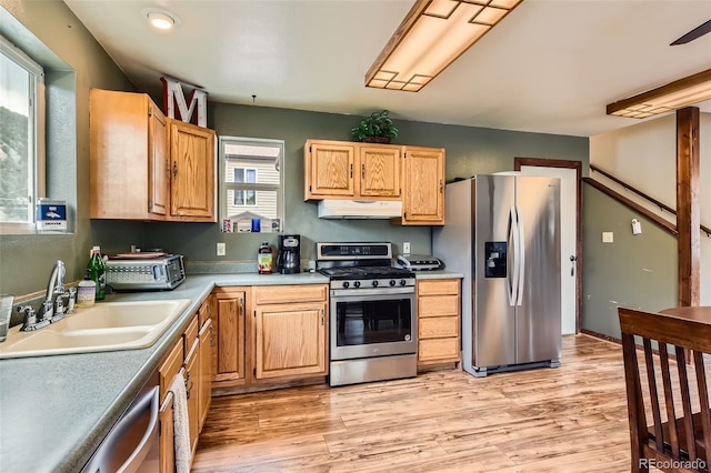 kitchen with appliances with stainless steel finishes, a sink, under cabinet range hood, light wood finished floors, and light countertops