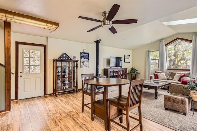 dining space with a wood stove, light wood-type flooring, a ceiling fan, and vaulted ceiling