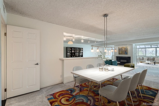dining space featuring a glass covered fireplace, a textured ceiling, carpet flooring, and baseboards