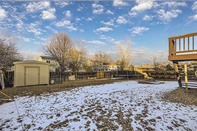 snowy yard with a deck, a storage unit, and a trampoline