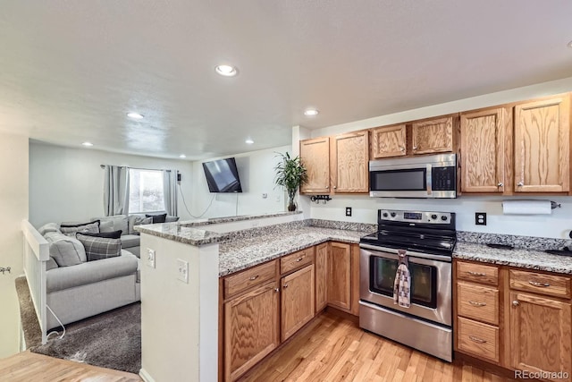 kitchen with kitchen peninsula, light stone countertops, appliances with stainless steel finishes, and light hardwood / wood-style floors