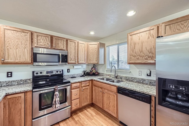 kitchen featuring stainless steel appliances, light stone counters, sink, and light wood-type flooring