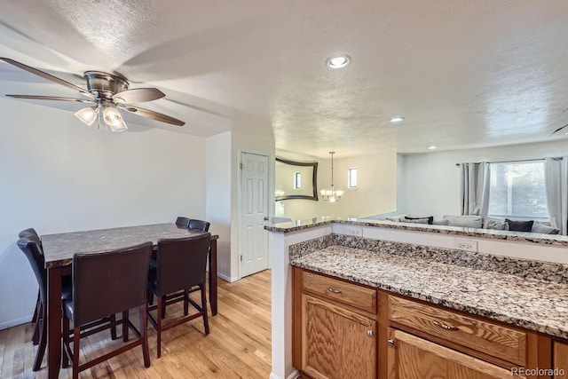 kitchen featuring light stone counters, a textured ceiling, hanging light fixtures, light wood-type flooring, and ceiling fan with notable chandelier