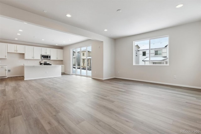 unfurnished living room with recessed lighting, light wood-style flooring, and baseboards