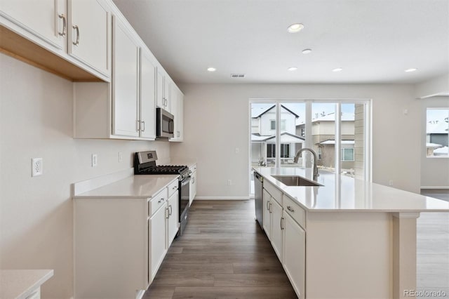 kitchen with wood finished floors, a kitchen island with sink, a sink, light countertops, and appliances with stainless steel finishes