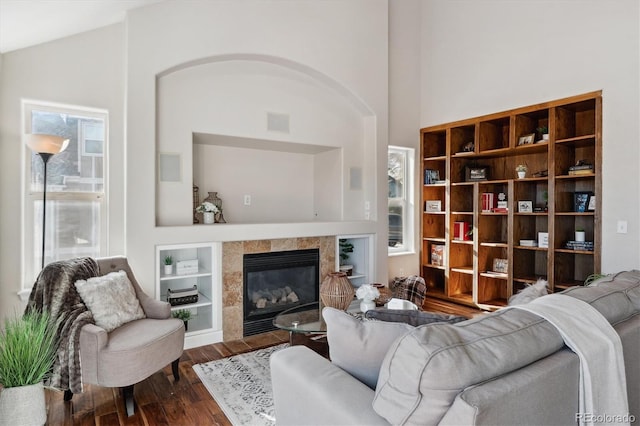 living room with dark hardwood / wood-style floors, built in features, lofted ceiling, and a tiled fireplace