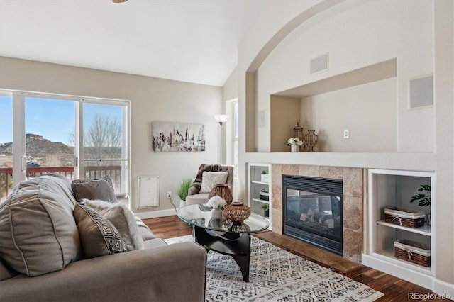 living room with lofted ceiling, wood-type flooring, a fireplace, built in features, and a mountain view