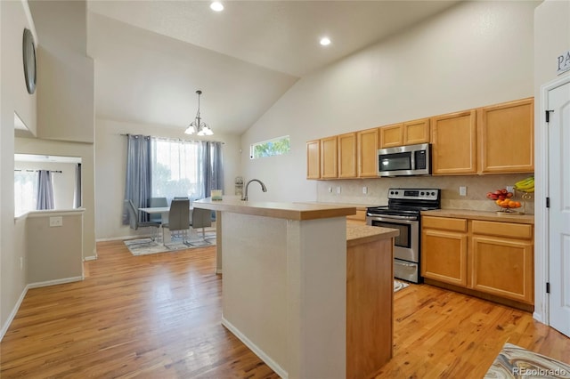 kitchen featuring light wood-type flooring, an island with sink, high vaulted ceiling, stainless steel appliances, and an inviting chandelier