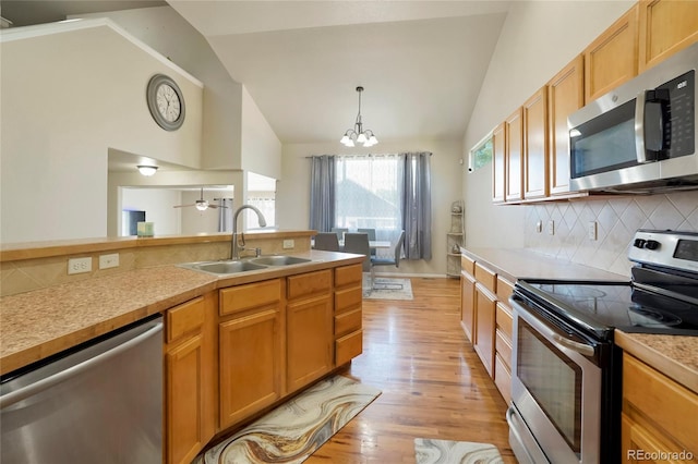 kitchen with appliances with stainless steel finishes, vaulted ceiling, sink, and light hardwood / wood-style flooring