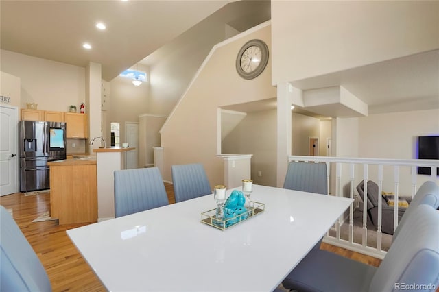 dining area featuring a high ceiling, sink, and light hardwood / wood-style flooring