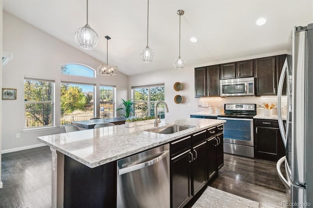 kitchen with stainless steel appliances, a sink, hanging light fixtures, dark brown cabinets, and an island with sink