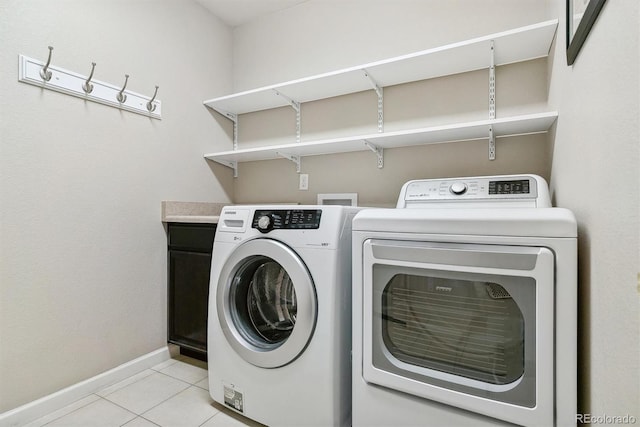 laundry area featuring light tile patterned floors, baseboards, washer and clothes dryer, and cabinet space