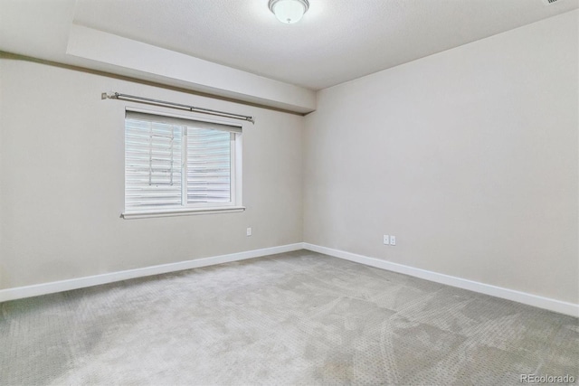 spare room with light colored carpet, a textured ceiling, and baseboards