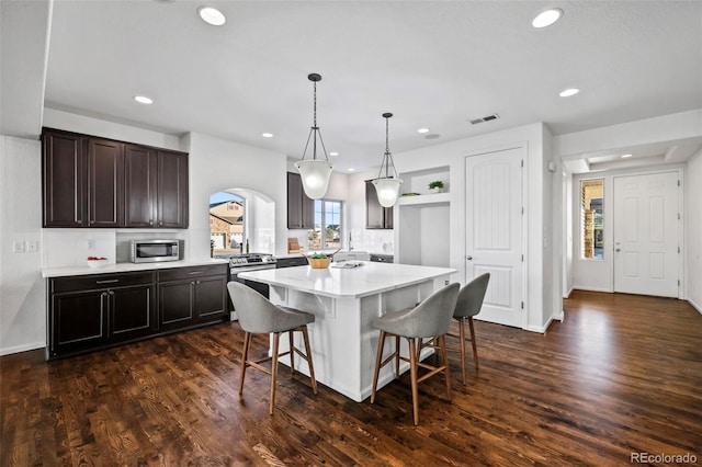 kitchen featuring dark wood-type flooring, hanging light fixtures, stainless steel appliances, and a kitchen island