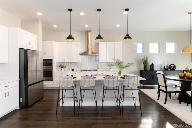 kitchen with stainless steel appliances, wall chimney range hood, and white cabinets