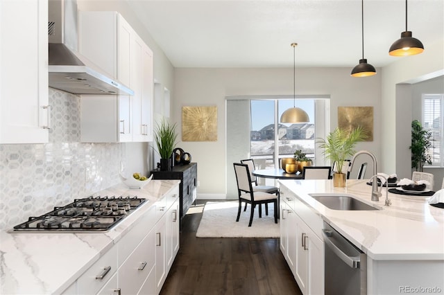 kitchen with appliances with stainless steel finishes, light stone countertops, pendant lighting, wall chimney exhaust hood, and white cabinetry