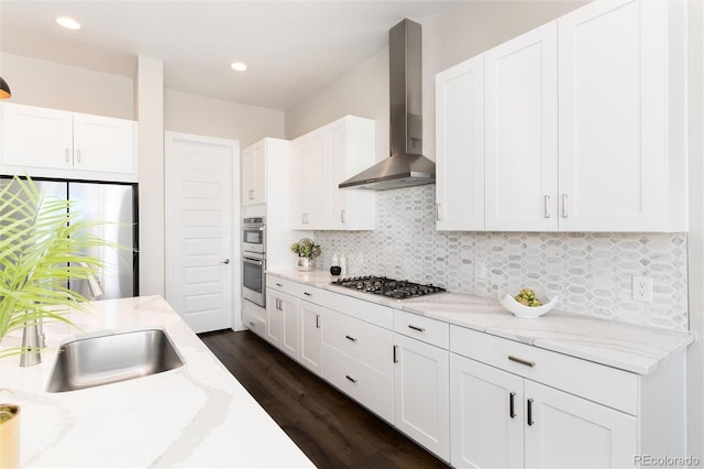 kitchen featuring white cabinets, light stone counters, backsplash, wall chimney range hood, and appliances with stainless steel finishes