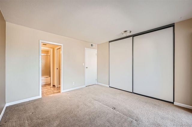 unfurnished bedroom featuring a closet, ensuite bath, and light colored carpet