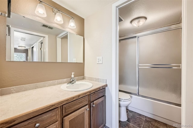 full bathroom featuring vanity, combined bath / shower with glass door, a textured ceiling, and toilet