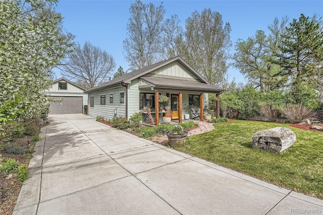 view of front of property featuring a detached garage, board and batten siding, a front yard, an outbuilding, and covered porch