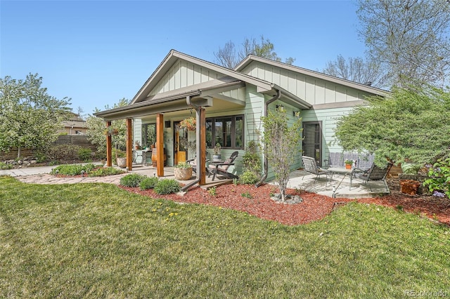 rear view of property featuring a lawn, fence, board and batten siding, and a patio area