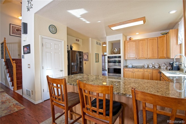 16873 Boreas Ct, Parker, CO 80134 - kitchen featuring stainless steel appliances, a peninsula, dark wood finished floors, a kitchen breakfast bar, and light stone counters
