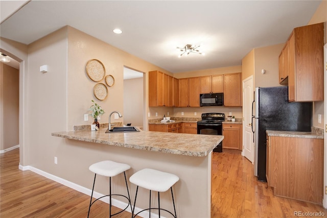 kitchen featuring a breakfast bar area, light wood finished floors, a peninsula, a sink, and black appliances