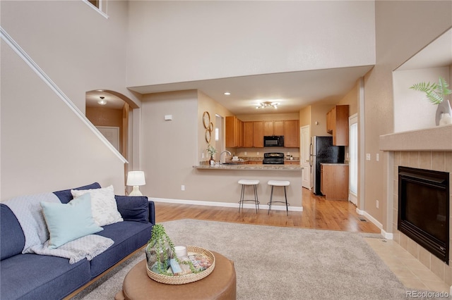 living area featuring arched walkways, light wood finished floors, baseboards, and a towering ceiling