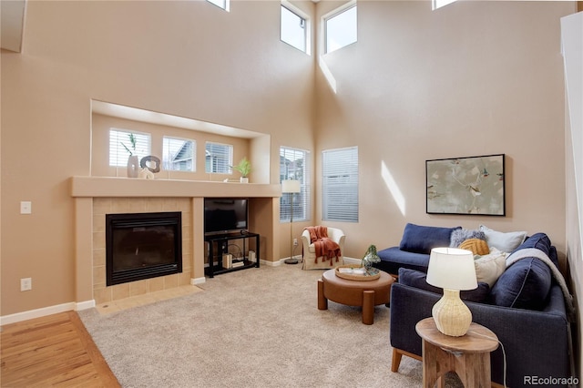 living area with wood finished floors, carpet flooring, a fireplace, baseboards, and a towering ceiling