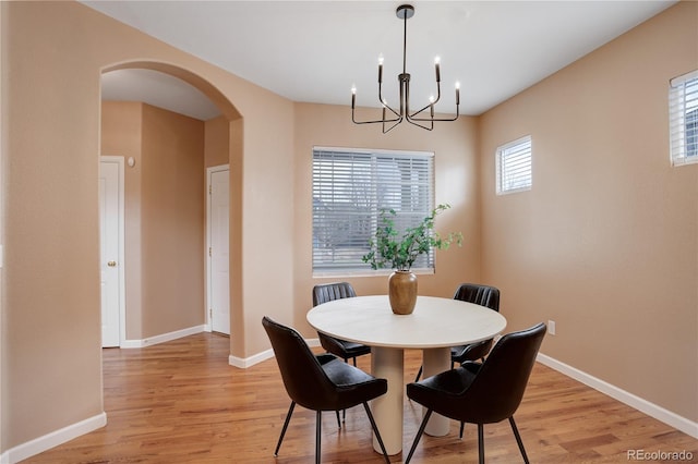 dining space with light wood-type flooring, arched walkways, baseboards, and a chandelier