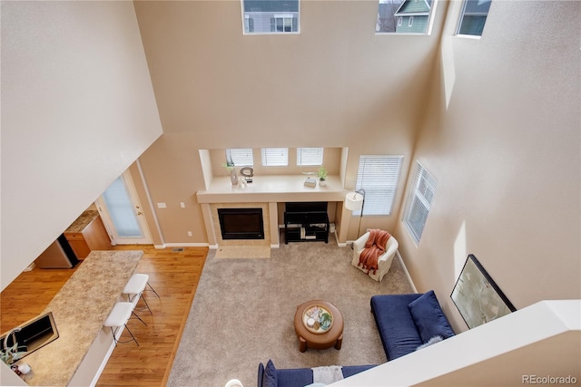 living room with a high ceiling, wood finished floors, baseboards, and a tile fireplace