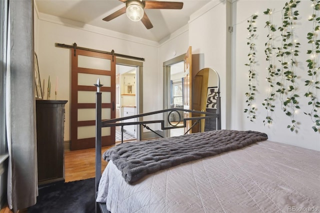 bedroom featuring a ceiling fan, dark wood-type flooring, a barn door, and ornamental molding