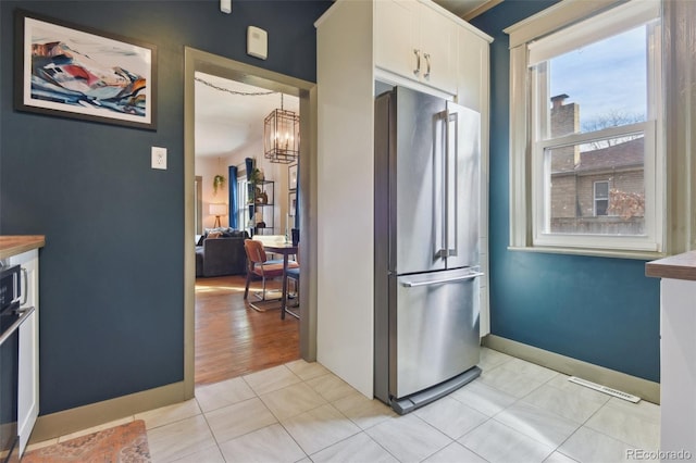 kitchen with baseboards, light tile patterned floors, a notable chandelier, high end fridge, and white cabinetry