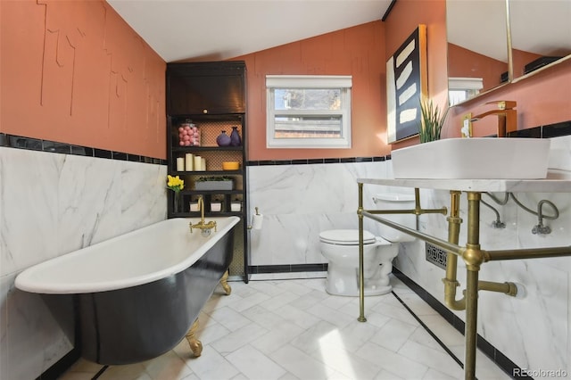 bathroom featuring a sink, a freestanding bath, vaulted ceiling, wainscoting, and toilet