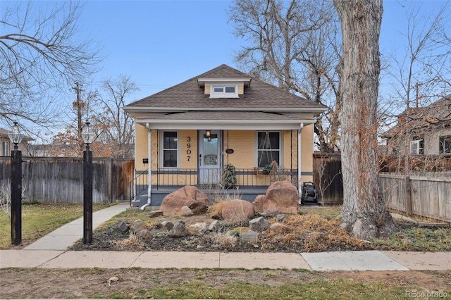 bungalow-style home with a porch, roof with shingles, and fence