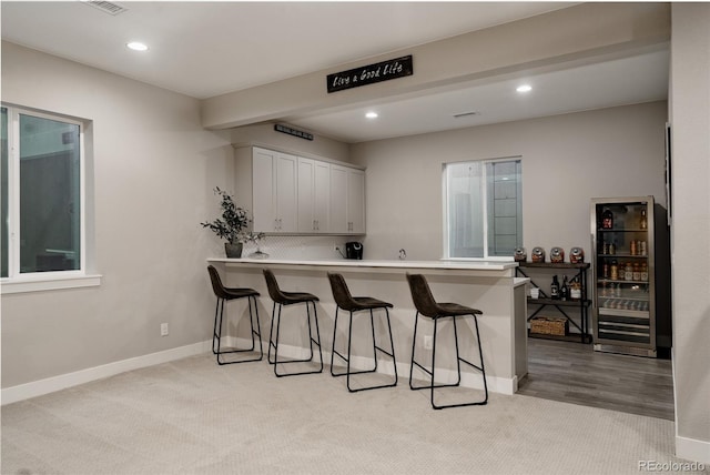 kitchen featuring white cabinetry, wine cooler, a kitchen breakfast bar, and kitchen peninsula