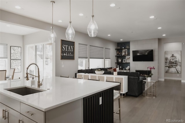 kitchen featuring pendant lighting, sink, a breakfast bar area, dark wood-type flooring, and a center island with sink