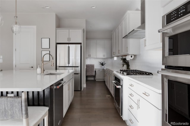 kitchen with stainless steel appliances, white cabinetry, pendant lighting, and wall chimney range hood