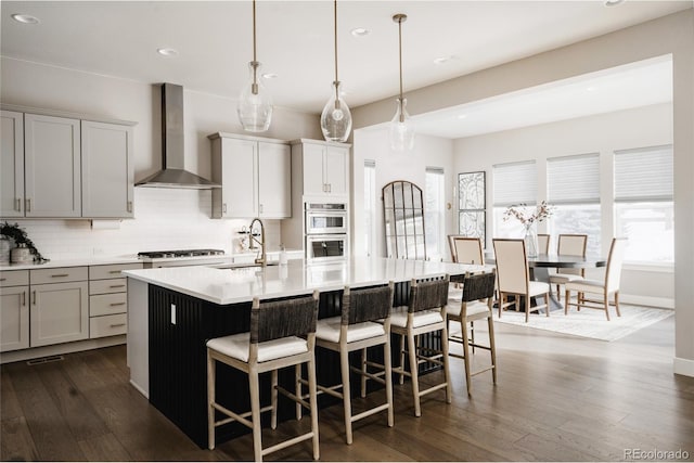 kitchen featuring sink, wall chimney exhaust hood, decorative light fixtures, and a kitchen island with sink