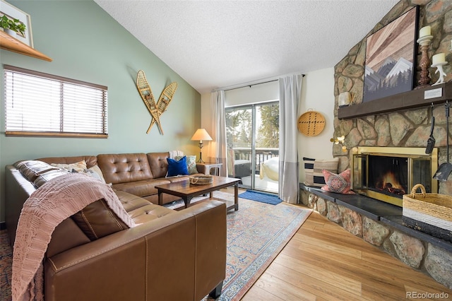 living room featuring vaulted ceiling, a fireplace, a textured ceiling, and light hardwood / wood-style floors