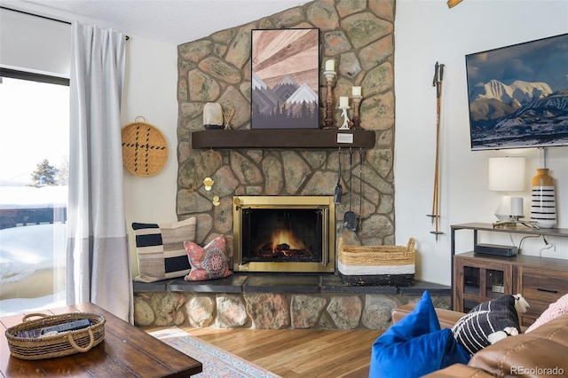 living room with a textured ceiling, hardwood / wood-style flooring, and a stone fireplace