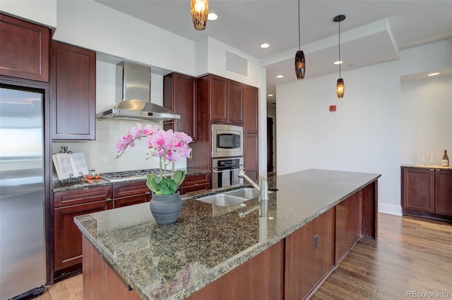 kitchen with a sink, wall chimney exhaust hood, reddish brown cabinets, and appliances with stainless steel finishes