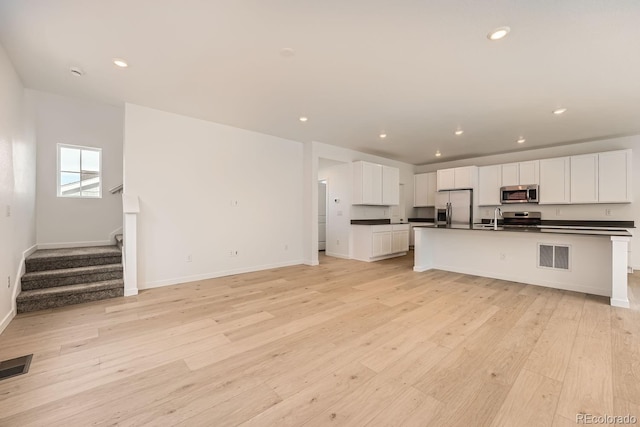 kitchen with an island with sink, appliances with stainless steel finishes, white cabinets, and light hardwood / wood-style flooring