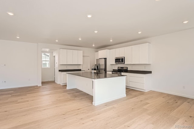 kitchen featuring white cabinetry, sink, stainless steel appliances, a center island with sink, and light wood-type flooring