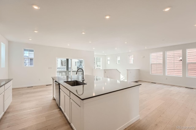 kitchen featuring sink, light hardwood / wood-style flooring, white cabinetry, a kitchen island with sink, and stainless steel dishwasher